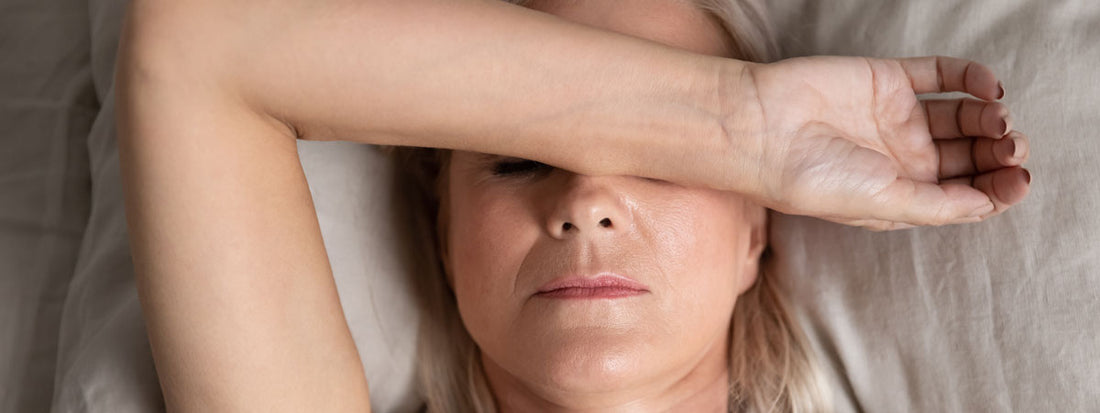 Woman resting on a bed, arm covering her face.